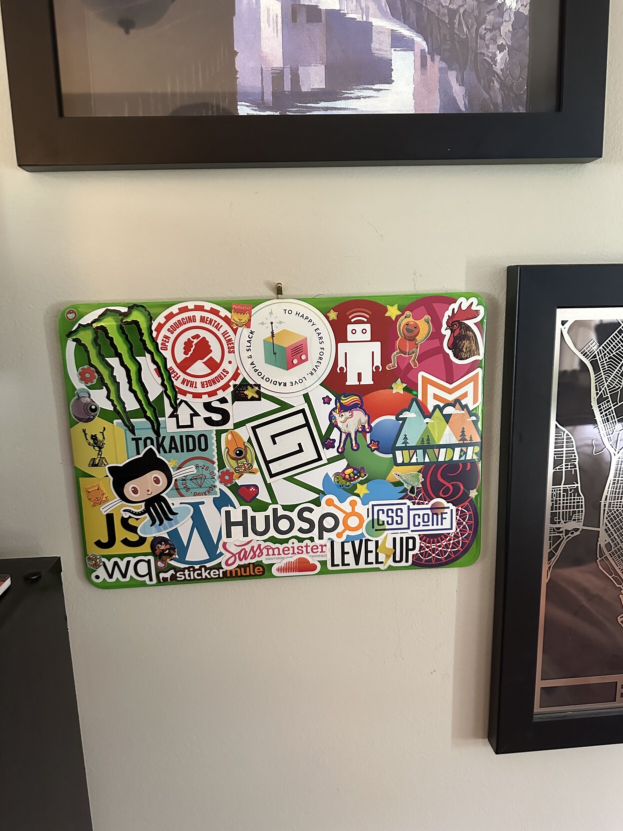 a photo of one of my old plastic laptop covers, covered in stickers, hanging on the wall with my paintings/photos framed around it. 