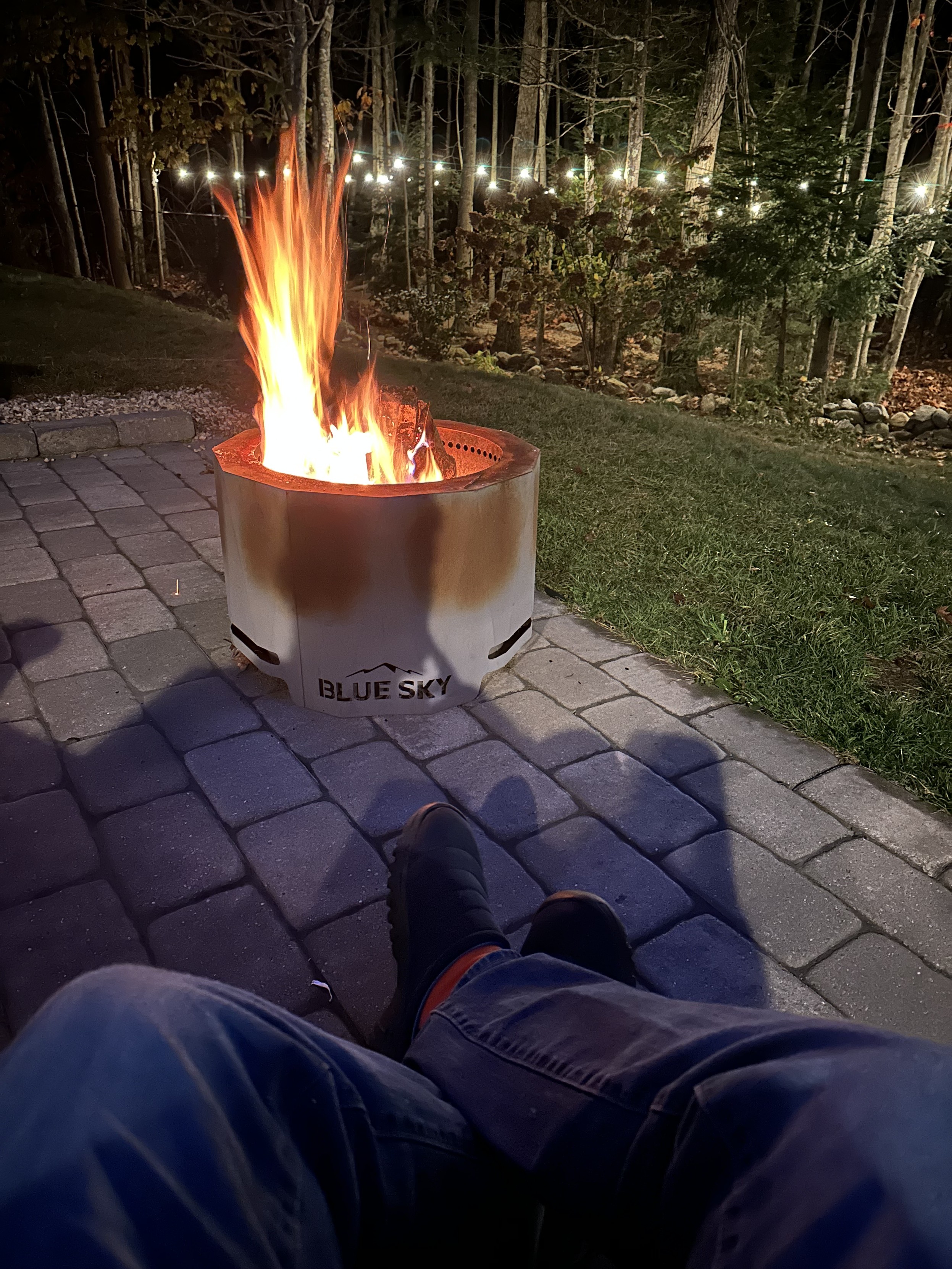 a photo of my fire pit on my
patio, with strings of lights in the woods beyond 