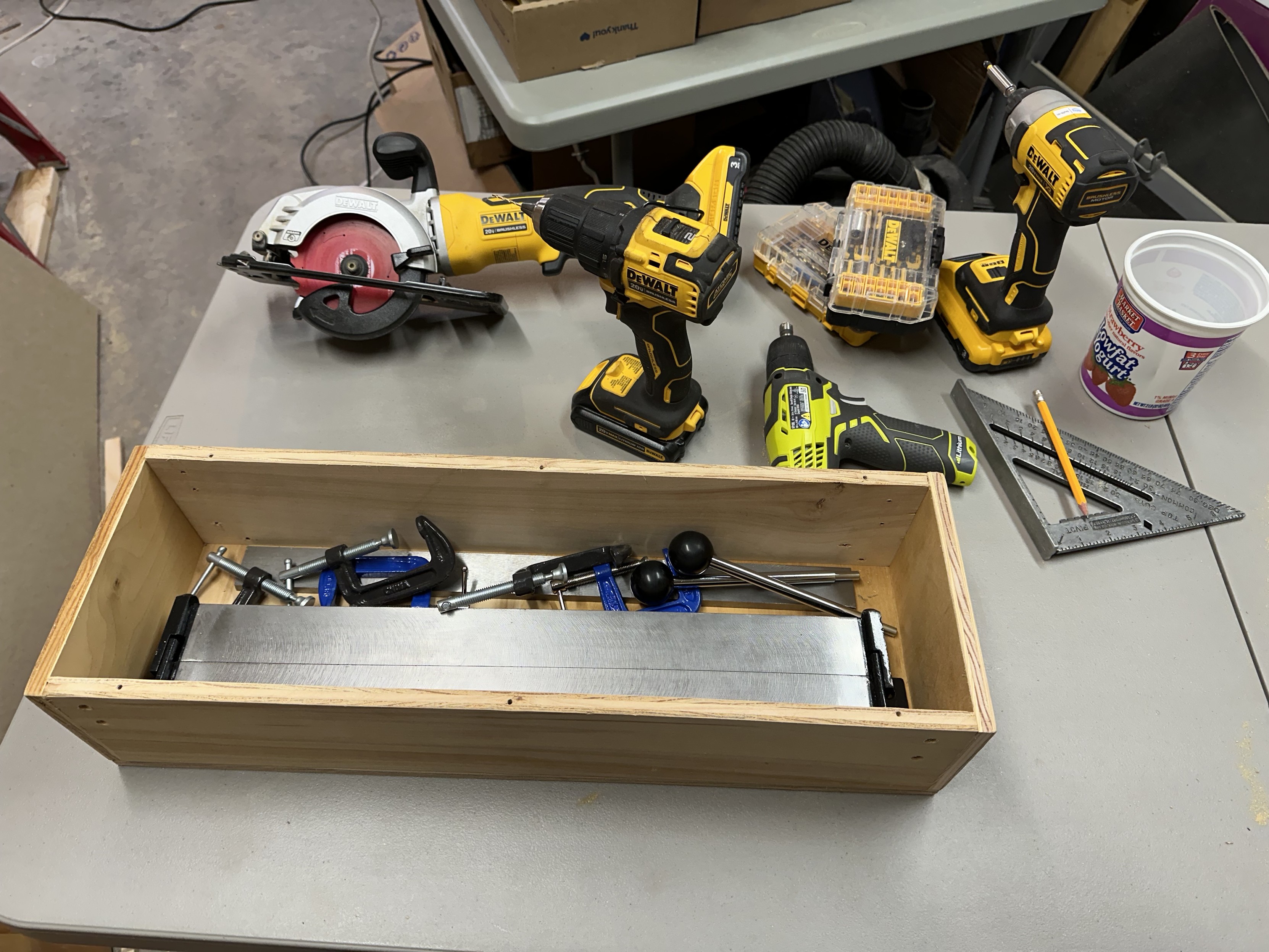 a photo of a plywood box i built, holding a sheet metal bender and some clamps. behind it are the hand tools i used to make it - a small circular saw, a drill with a small drill bit, a drill with a countersinking drill bit, and a drill/driver