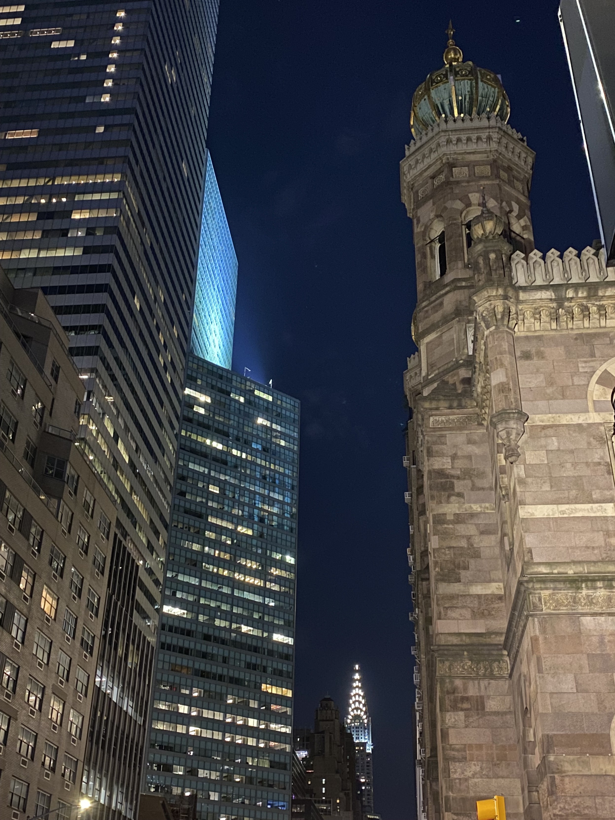a photo down Lexington Avenue in NYC at night, with a lit up Central Synagogue in the foreground and the Chrysler Building in the distance