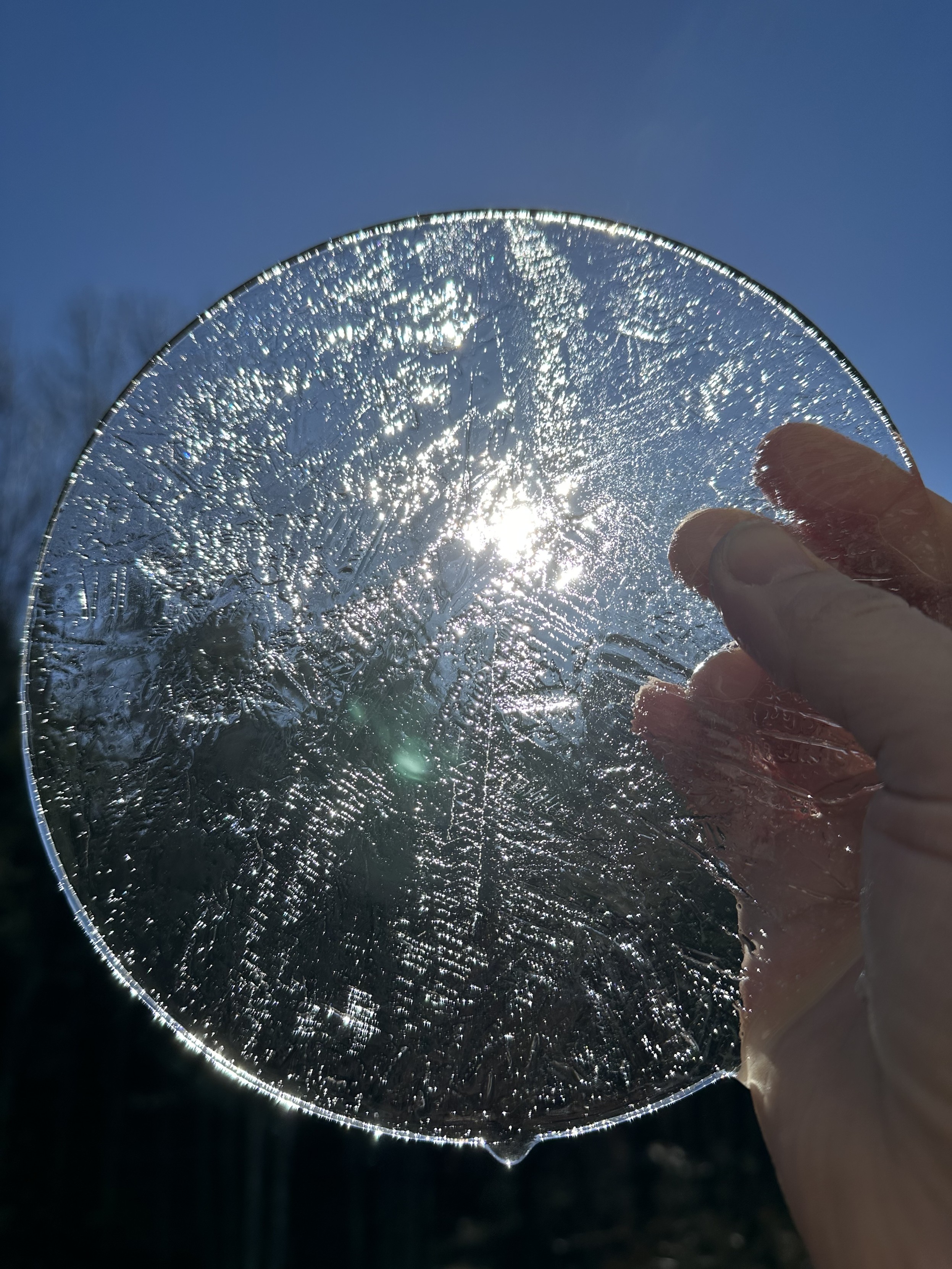 a round sheet of ice being held up so the sun can shine through it