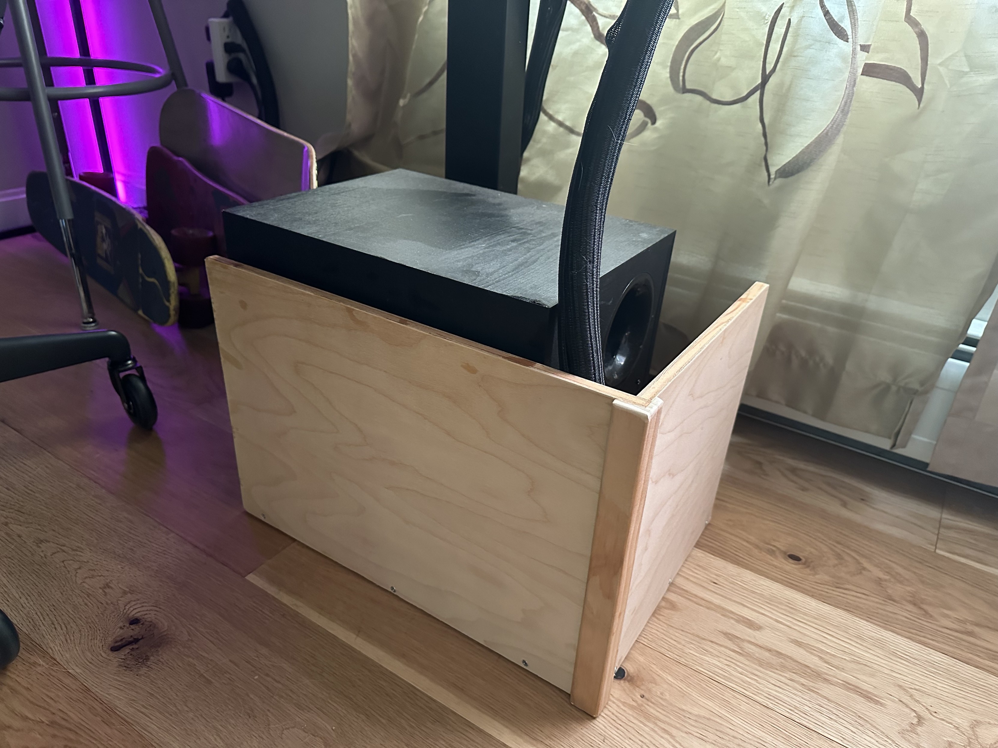 a photo of a small plywood half-box under and around the subwoofer underneath my desk 