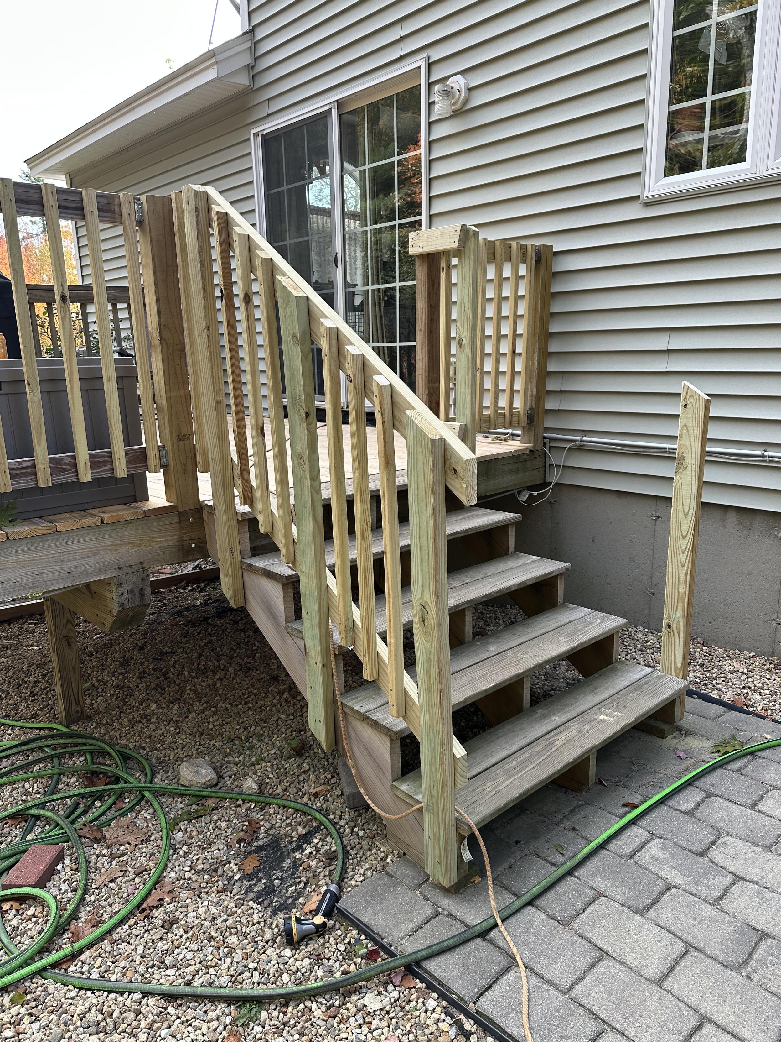 a photo of a railing on the left side of a set of 5 stairs down from a deck to a patio and only a couple of pieces of railing attached to the right side.