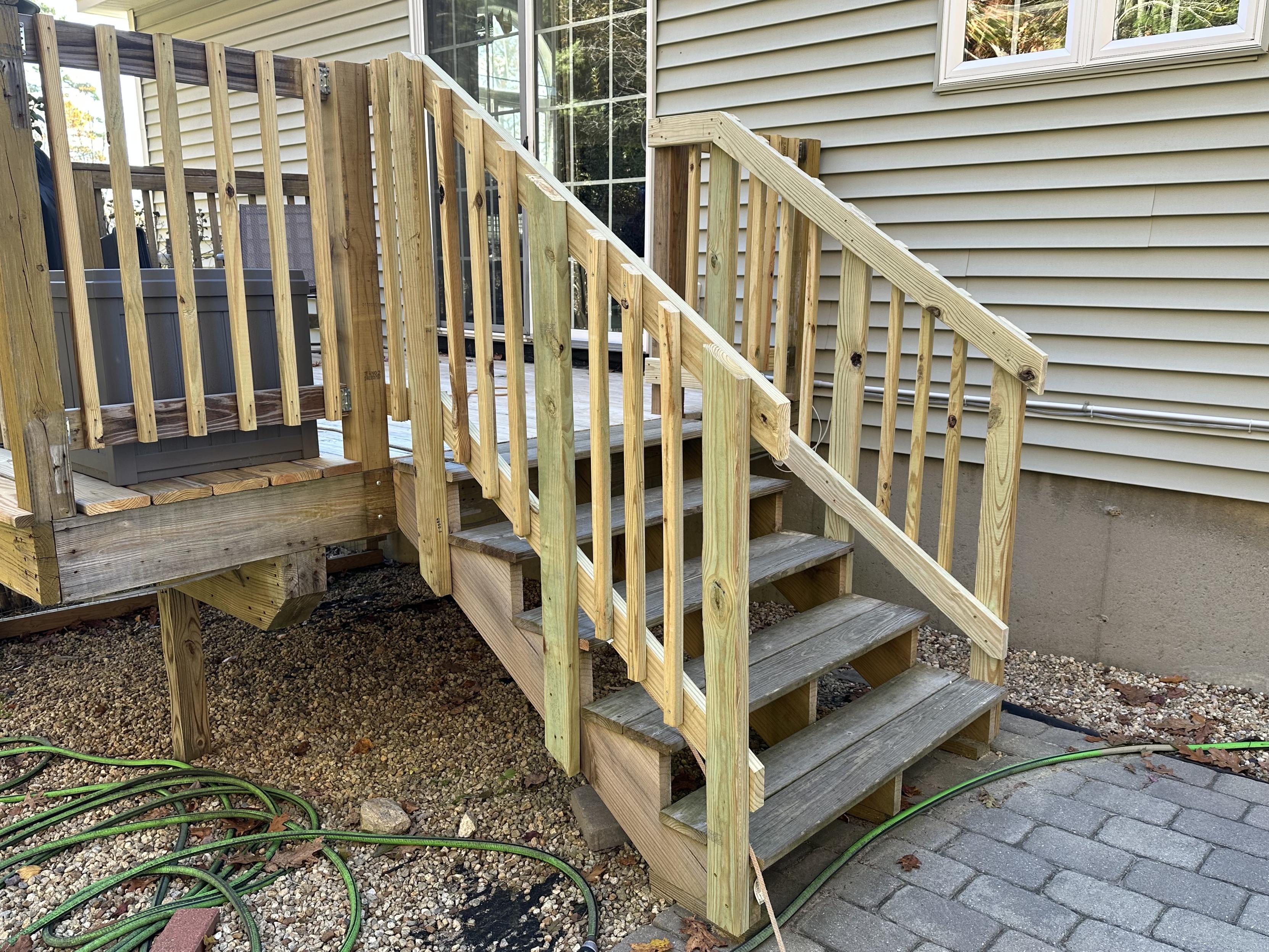 a photo of a set of stairs leading down from a deck to a patio, with newly installed railings on both sides, fitted with balusters.