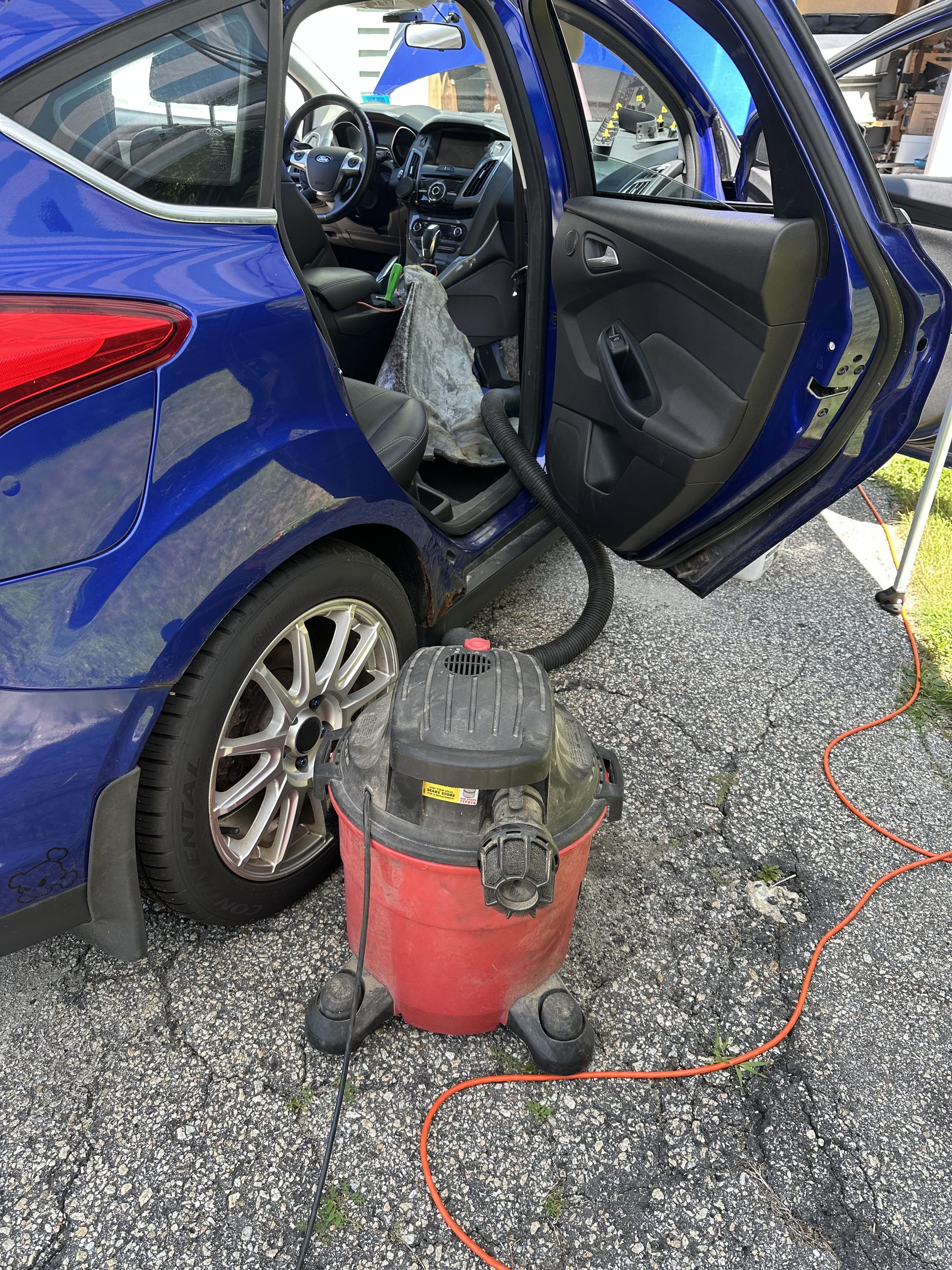 A photo of my car with the passenger seat removed the carpet, pulled backwards and a shop vac in the foreground ready to sop up as much water/moisture as it can